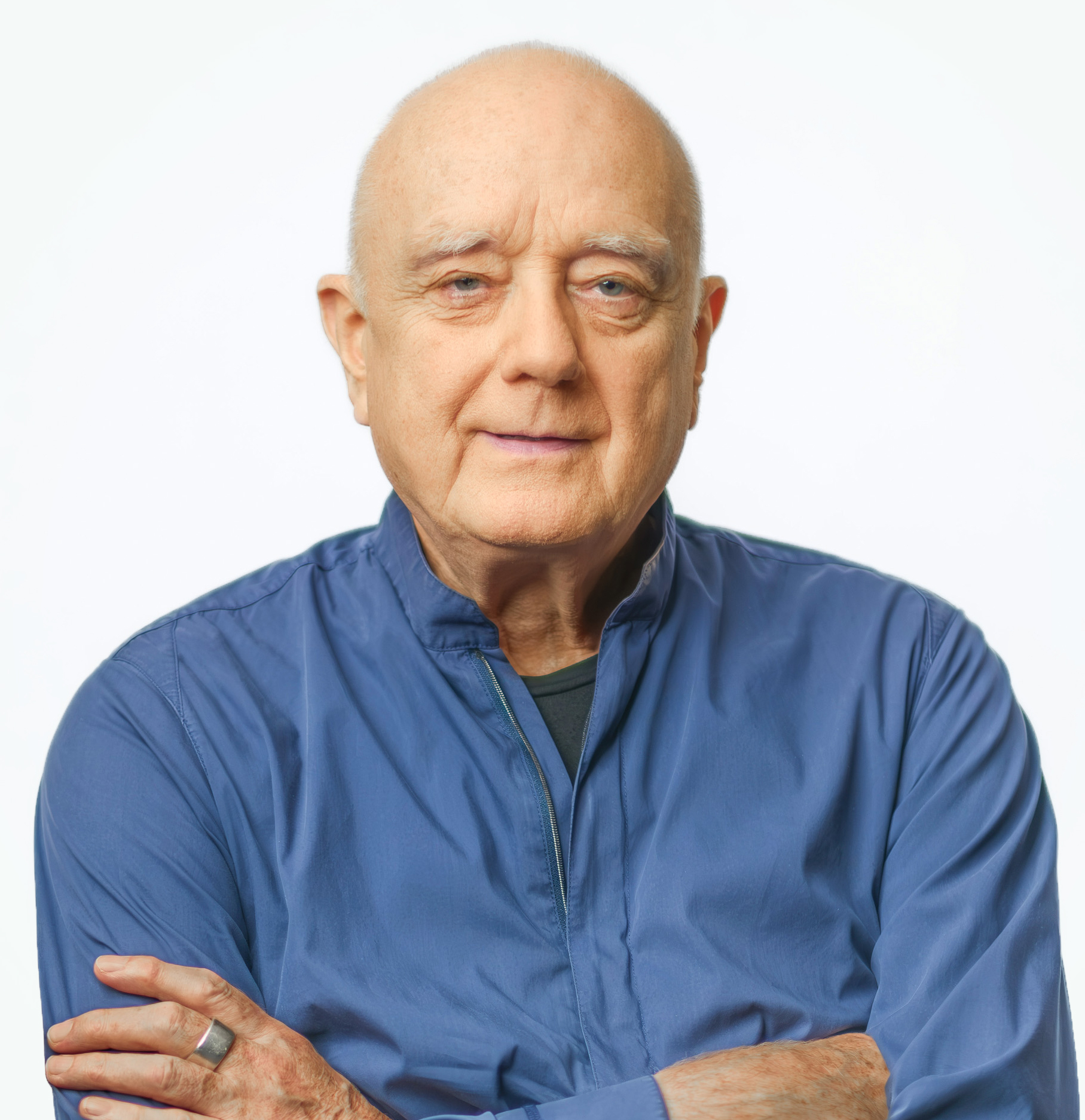 Portrait eines kahlköpfigen älteren Herrn in einem blauen Hemd und mit verschränkten Armen.