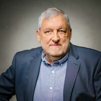 Lutz Fischmann Portrait eines älteren Herrn mit kräftiger Statur und Dreitagebart in einem blauen Jackett und hellblauem Hemd.