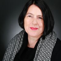 Portrait einer Dame mit dunklen kinnlangen Haaren, rotem Lippenstift, schwarzen Pullover und schwarz-weißem Schal mit Rautenmuster.