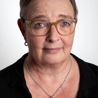 Dr. Anke Schierholz Portrait einer Frau mit Brille und kurzen Haaren. Sie trägt ein schwarzes Oberteil mit Spitze und eine auffällige Silberkette mit zwei Perlenanhängern.