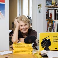 Eine Frau stützt sich auf einen Stapel gelber Bücher und lacht in die Kamera. Auf dem Schreibtisch steht ein mit dem Buchcover bezogener Laptop. Darauf steht: "Imogen Kimmel, Bettina Schoeller Bouju, Barbara Teufel: Anleitung für eine Rebellion. 12 Regisseurinnen schreiben Geschichte". Im Hintergrund eine offene Schiebetür, rechts davon ein schmales Bücherregal, links ist der untere Teil eines Plakats zu sehen. Auf dem Ausschnitt ist der britische Union Jack abgebildet sowie die Schrift: "Ein Film über die Liebe, übers Dicksein und den Traum, dass jeder eine Chance hat" sowie "MAKE YOUR FAT FUNCTIONAL".